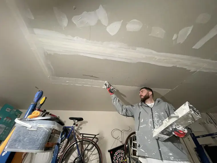 Houseworks crew member smoothing a drywall ceiling repair