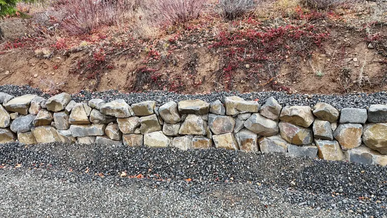 Close aerial view of a boulder rockery wall along a gravel drive